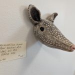 A detailed clay bust of an armadillo with a hand-written description, "Armadillos have four babies at a time, all the same sex."