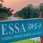 a picture of the Eureka Springs School of the Arts sign with the sunset in the background framed by a road in the background