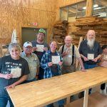 A group of people in a wood studio holding up kumiko tiles