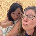 Two women making silly faces sitting on river rocks with a river in the background