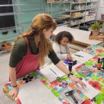 Instructor guiding a young student during a printmaking activity in ESSA’s Young Artist Program