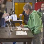 Participant in a green hoodie filling out a form at a workshop table while others gather nearby.