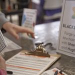 Close-up of a blacksmithing activity sign and sign-up sheet on a worktable with tools and materials.