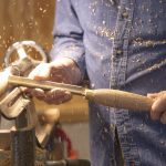Woodturner using a chisel on a spinning lathe as wood shavings fly through the air.