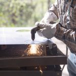 Person using a plasma cutter to cut metal, with bright sparks flying from the surface.
