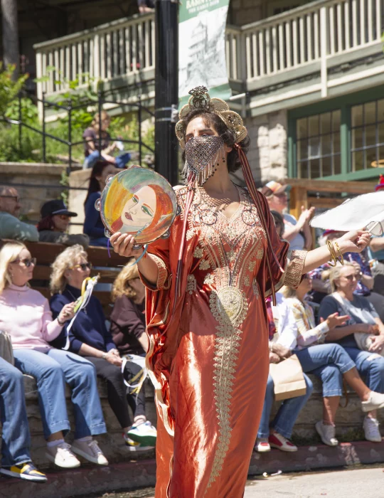Costumed performer wearing an ornate orange gown and decorative face covering during the ArtRageous Parade in Eureka Springs, Arkansas.