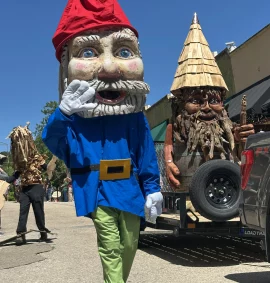 Giant gnome character and carved wooden gnome figure moving through the ArtRageous Parade in downtown Eureka Springs, Arkansas.