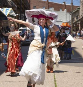 Women of the World parade participants dancing in colorful costumes during the ArtRageous Parade in downtown Eureka Springs, Arkansas.