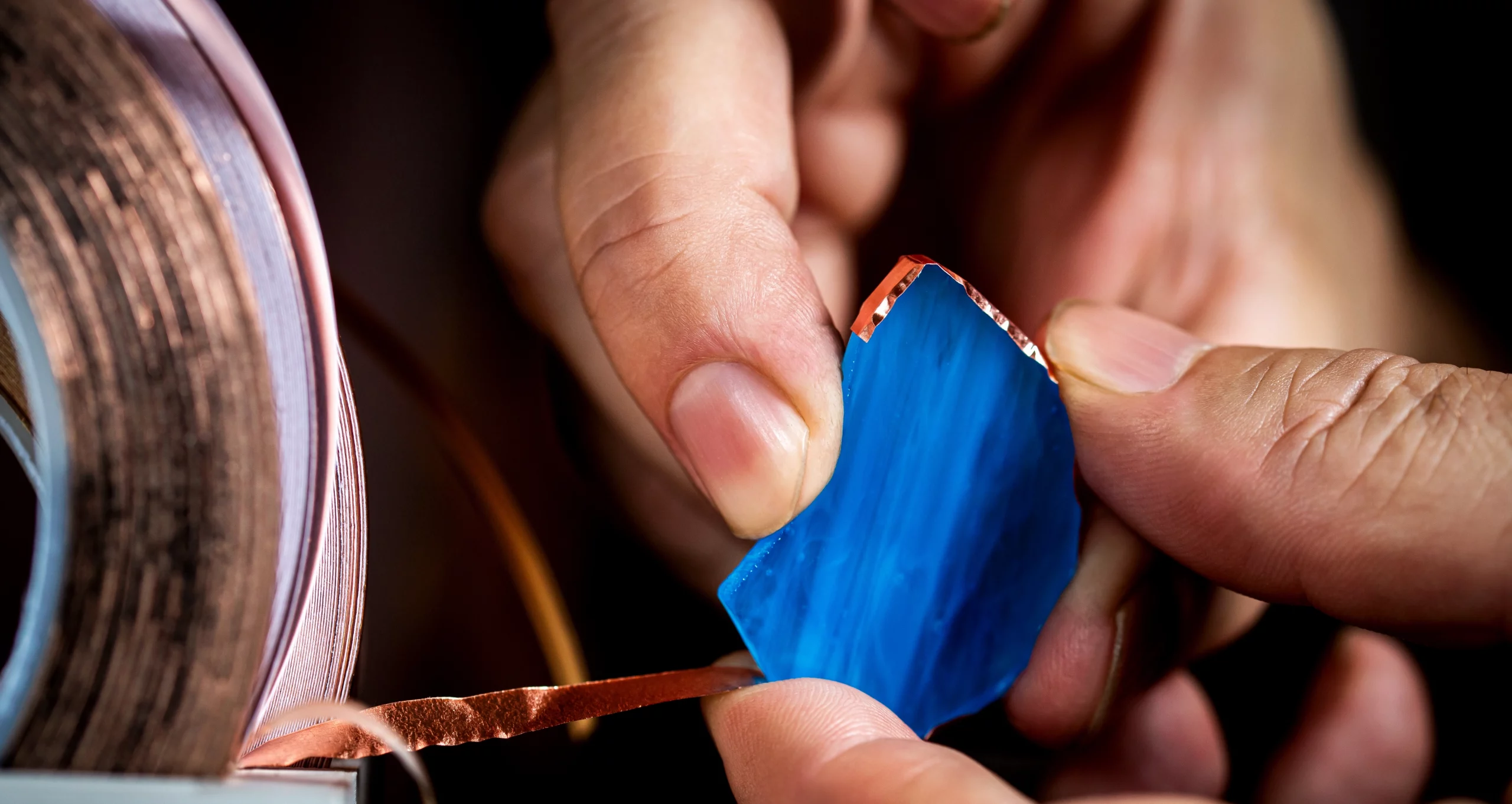 Close-up of an artist applying copper foil to a blue stained glass piece.