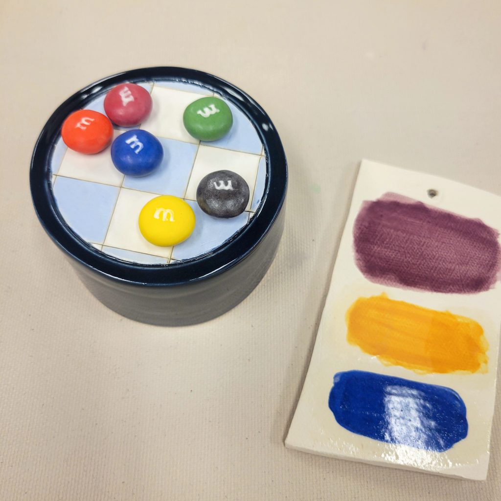 Colorful ceramic M&M-style candies arranged on a blue-and-white tiled form beside purple, yellow, and blue color tests.