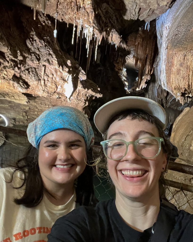 Erin Harris and Kaitlyn Cirielli smile for a selfie inside a cave surrounded by stalactites and rock formations.