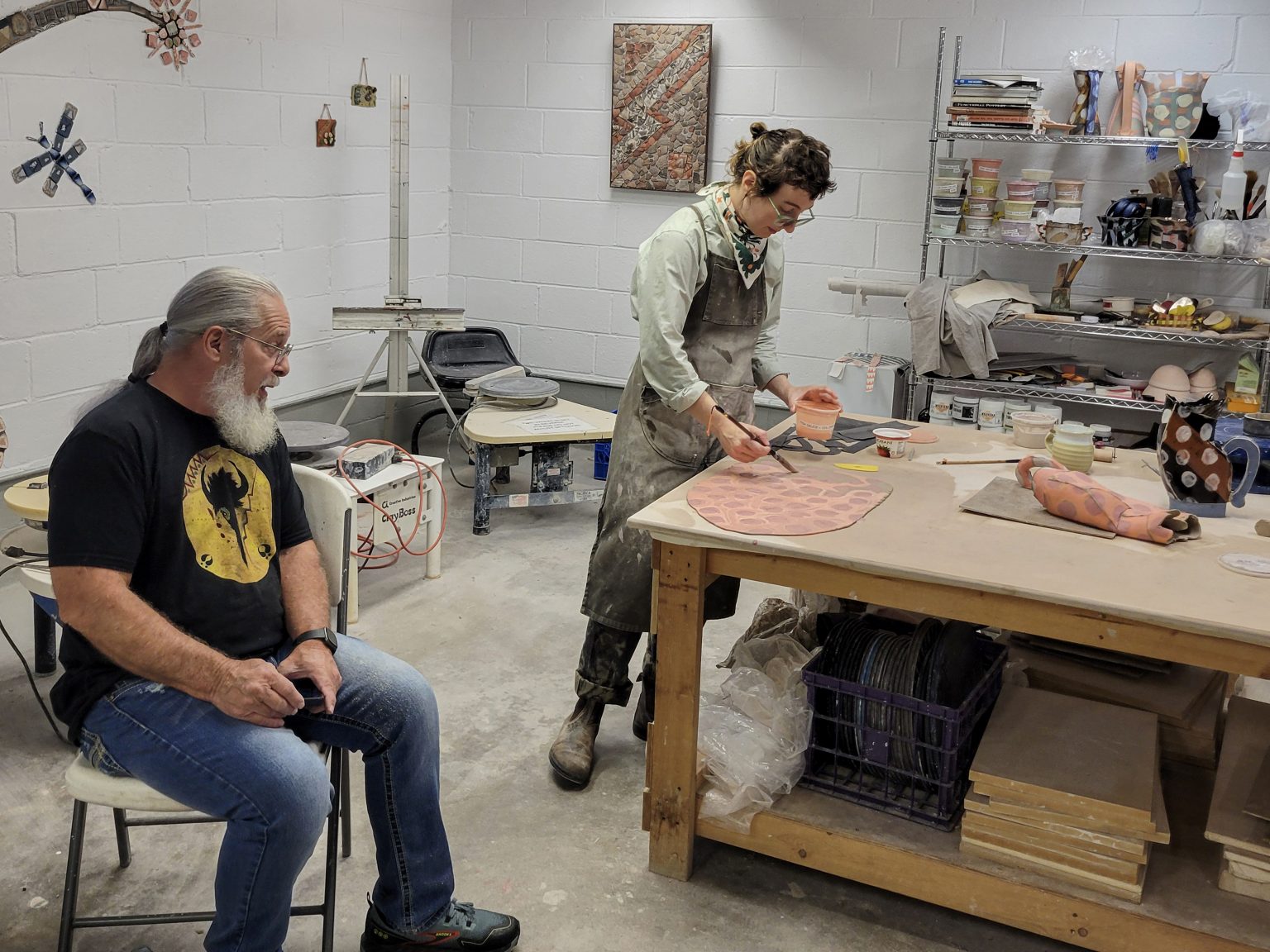 A guest chats with Kaitlyn Cirielli as she paints a patterned clay slab in the ESSA Ceramics Studio.