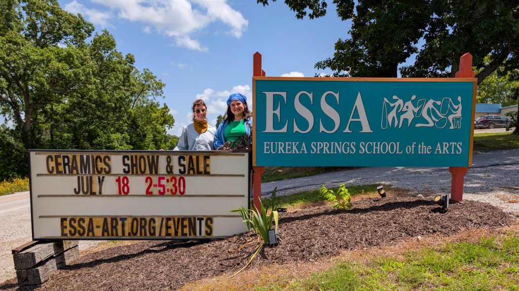 Kaitlyn Cirielli and Erin Harris stand behind a marquee advertising their ceramics show and sale beside the ESSA campus sign.