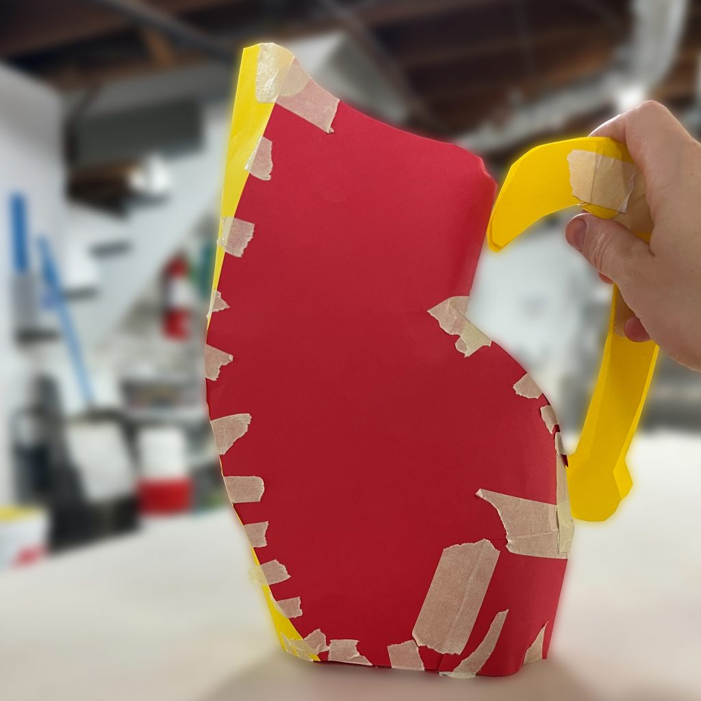 Red and yellow paper template shaped like a pitcher and held together with tape in the ESSA Ceramics Studio.