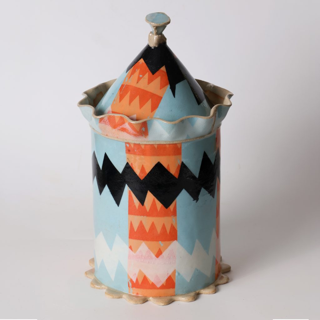 Lidded ceramic vessel by Kaitlyn Cirielli with blue, orange, black, and white geometric patterns and a scalloped rim.