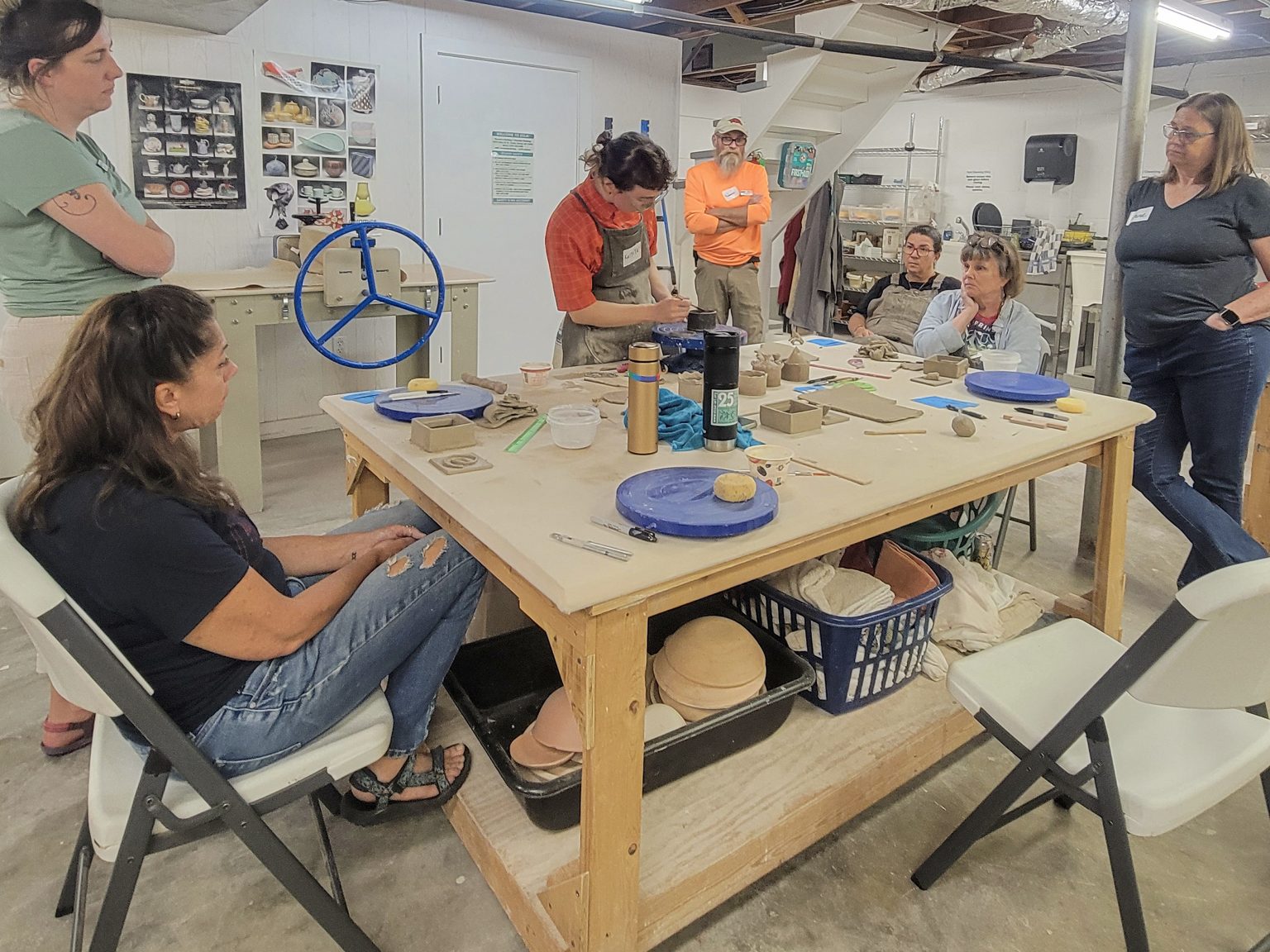 Kaitlyn Cirielli demonstrates a tarpaper clay-construction technique for ESSA staff gathered around a ceramics worktable.
